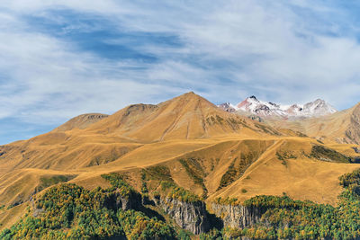 Autumn in the mountains, high sky with clouds, snow-capped mountain peaks. 