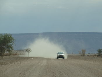 Car on road amidst field against sky