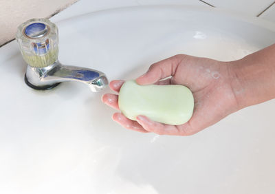 Cropped person washing hand with soap bar at sink