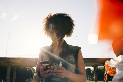 Young man with electronic cigarette using mobile phone in summer