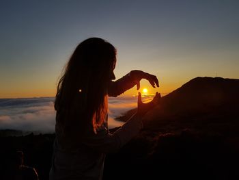 Woman standing by tree against sky during sunset