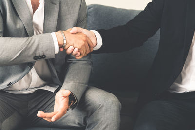 Midsection of business people shaking hand while sitting on sofa at office