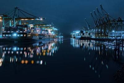 Illuminated commercial dock reflecting on sea against sky at night