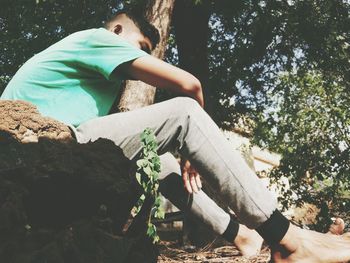 Side view of man sitting by plants against trees