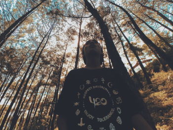 Rear view of man standing by tree trunk in forest