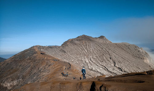 Rear view of woman walking on mountain against blue sky