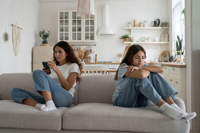 Young woman using phone while sitting on sofa at home