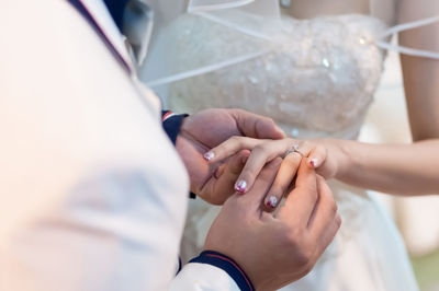 Midsection of groom putting ring on bride finger during wedding ceremony