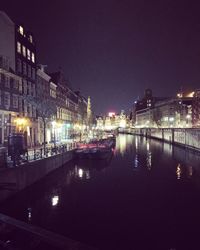 Illuminated city by river against sky at night