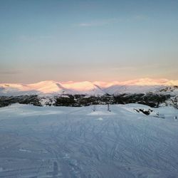 Snow covered landscape against sky during sunset