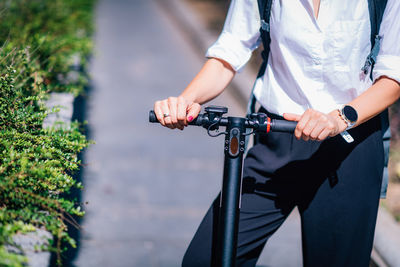 Midsection of woman with electric scooter standing on footpath