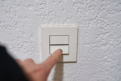 Cropped hand of person holding electric lamp on wall