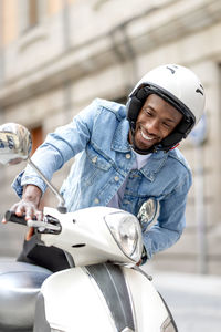 Young man wearing crash helmet while getting on scooter
