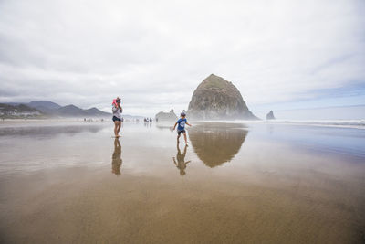 Mother watches as son runs along wet sand beach near haystack rock.