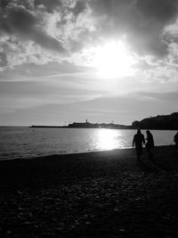 Silhouette couple standing on beach against sky during sunset