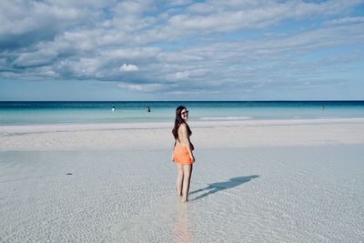 Rear view of woman standing at beach against sky