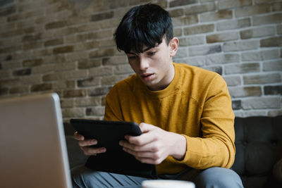 Man using mobile phone while sitting on wall