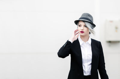 Thoughtful businesswoman wearing hat standing against wall