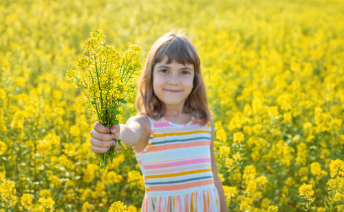 Portrait of cute girl holding flowers while standing in field