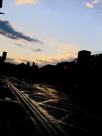Road by silhouette buildings against sky during sunset