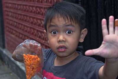 Close-up portrait of shocked boy holding snacks in plastic