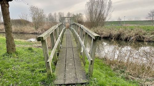 Footbridge over canal amidst trees against sky