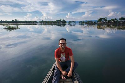 Portrait of man sitting in boat on lake against sky