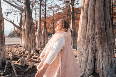 Woman standing by tree trunk in forest