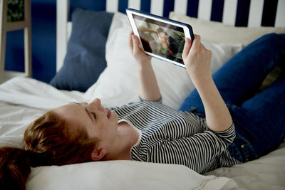 Smiling woman video conferencing with friend while lying on bed at home