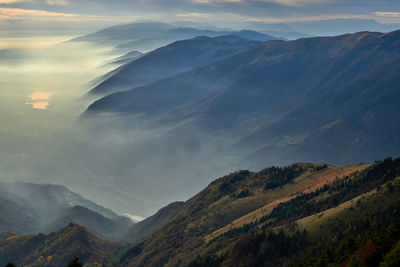 Scenic view of mountains with mist against cloudy sky