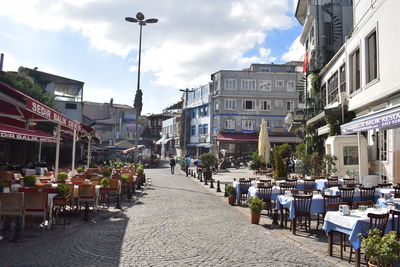 Empty chairs and tables at sidewalk cafe amidst buildings in city