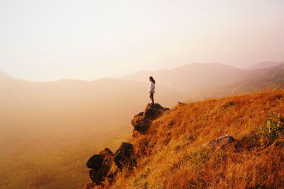 Side view of woman standing on mountain against sky during sunset