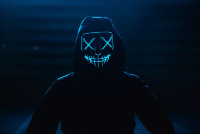 Portrait of man wearing glowing mask standing against black background