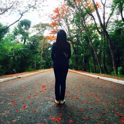 Rear view of woman standing on road amidst trees