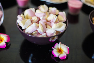 Close-up of marshmallows in bowl by flowers on glass table