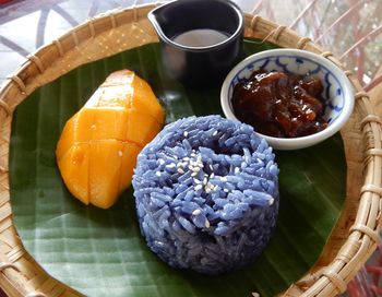 High angle view of mango fruit, blue sticky rice and marmalade with cream, served in a basket .