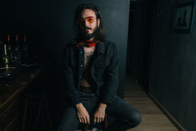 Portrait of man sitting on stool against wall