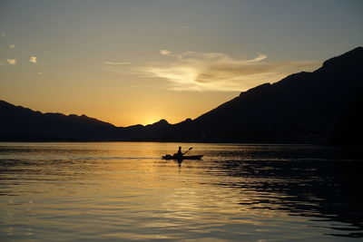 Silhouette person in sea against sky during sunset