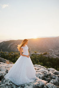 Rear view of woman sitting on rock against sky