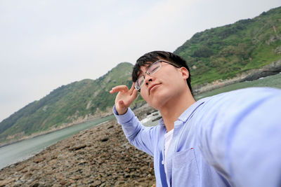 Portrait of young man standing on mountain against sky