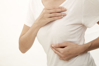 Midsection of woman adjusting breast against white background