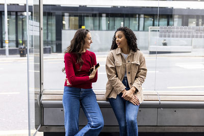 Woman talking with friend sitting at bus stop