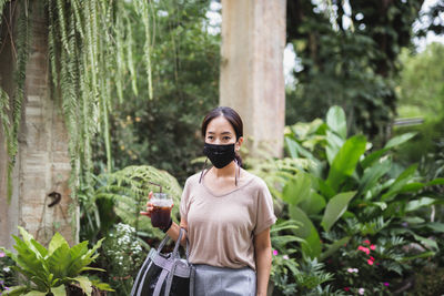Portrait of woman in protective mask standing against plants