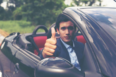 Portrait of confident young businessman showing thumbs in car on road
