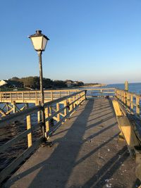 Street light on footpath by sea against clear sky