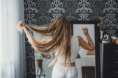 Rear view of woman looking at mirror while holding hair