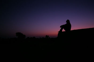 Side view of silhouette woman sitting against dramatic sky during sunset