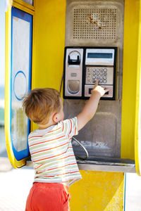 Rear view of boy standing at telephone booth