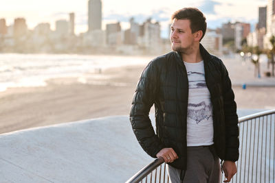 Young man looking away while standing by railing