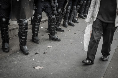 Low section of man walking by armed forces on street in city